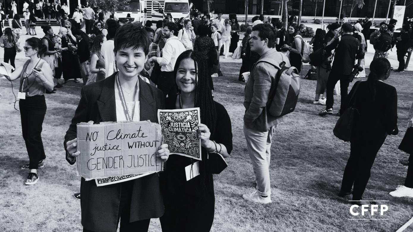 Two women, CFFP Project Manager Sheena and ex-fellow Michelle, stand together in a crowd of protesters at COP27, holding signs that read 'Climate Justice Now' and 'No Climate Justice withour Gender Jsutice' and 'Justicia Climatica". The are standing in the middle of a crowd at COP27.